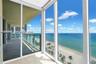 Covered balcony featuring floor-to-ceiling glass paneling, tile flooring, and metal railing overlooking the coastline