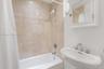 Full-height stone tile shower surround, pedestal sink with polished chrome fixtures, and white wall-mounted medicine cabinet