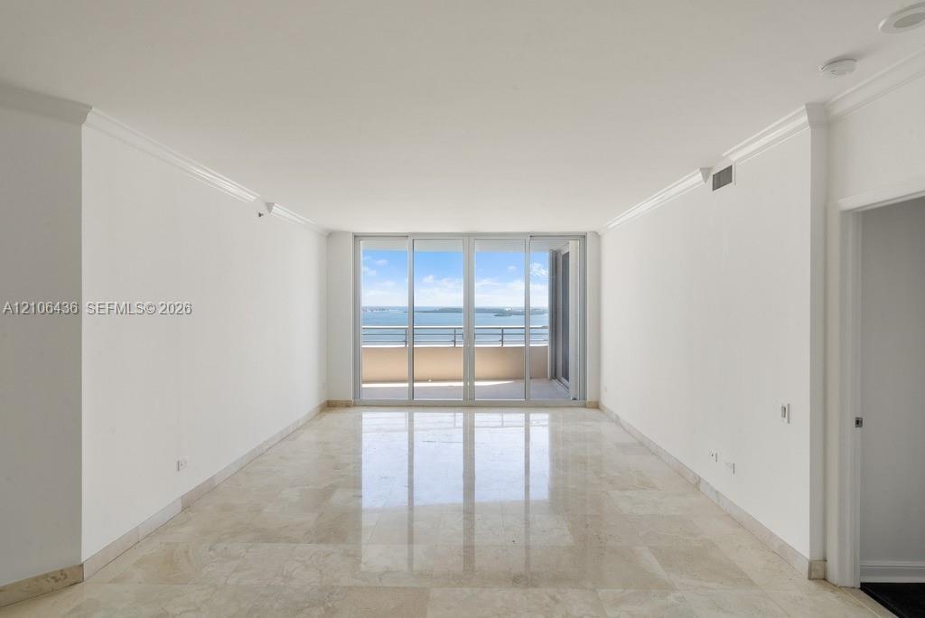 Living area featuring polished stone flooring, crown molding, and floor-to-ceiling glass sliding doors opening to a private balcony