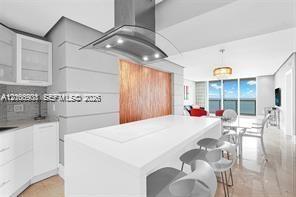 Kitchen featuring a central island with a solid-surface countertop, stainless steel overhead range hood, white cabinetry, wood-finish paneling, and po