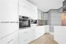 Modern kitchen featuring high-gloss white cabinetry, integrated stainless steel appliances, recessed lighting, and wood-finish flooring