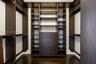 Custom walk-in closet featuring dark wood-finish cabinetry, integrated open shelving, a center bank of five soft-close drawers with metallic pulls, an