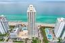 High-rise coastal residential tower featuring multi-story glass balconies, ground-level outdoor swimming pools, and direct oceanfront access