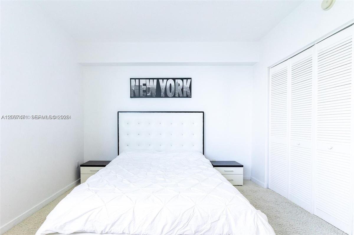 Neutral-toned carpeting, white walls, and a built-in closet with white louvered doors