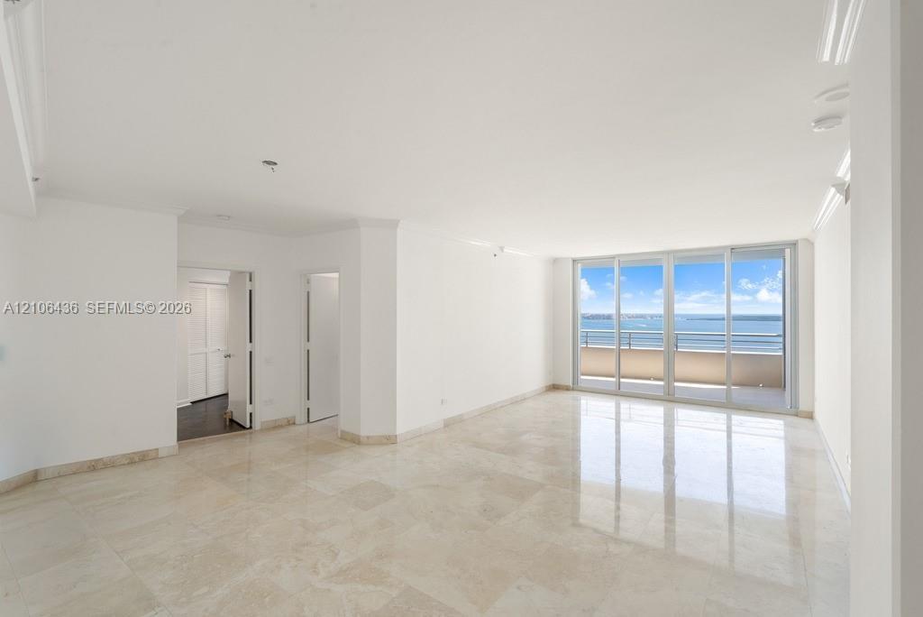 Open-concept interior featuring light-toned stone tile flooring, crown molding, and floor-to-ceiling glass sliding doors providing water scenery and a
