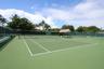 Hard-court tennis facility featuring perimeter fencing and a thatch-roofed cabana