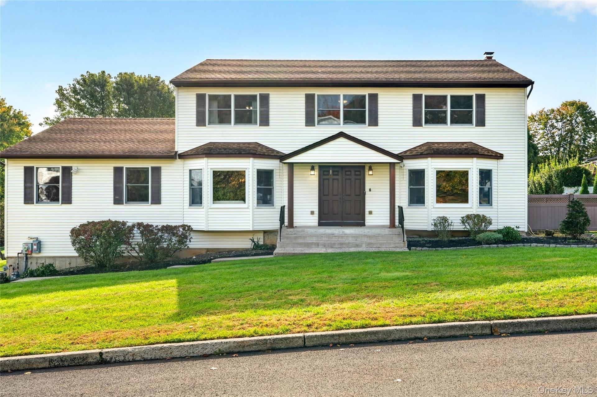 Two-story exterior featuring  vinyl siding, dark-toned shutters, a covered front entryway with double doors, symmetrical bay windows, and a shingled r