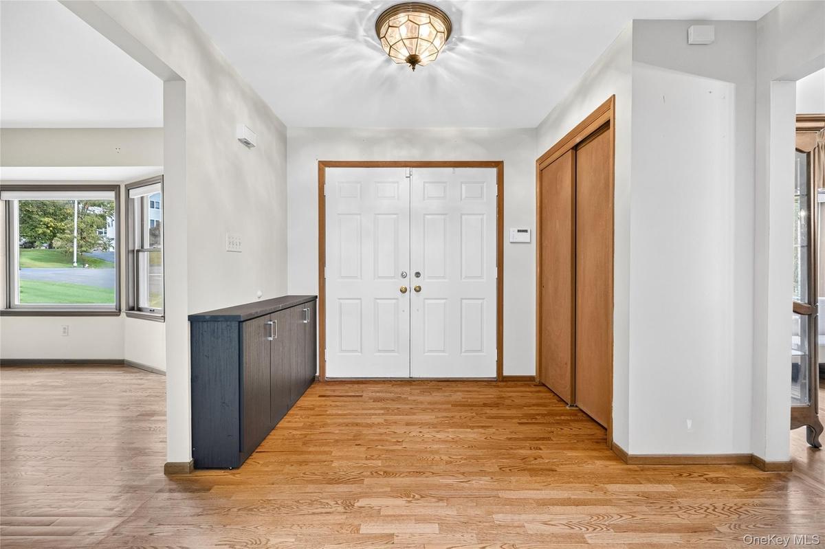 Foyer featuring wood-finish flooring, double-door entryway, built-in storage cabinetry, sliding-door closet, and overhead decorative lighting