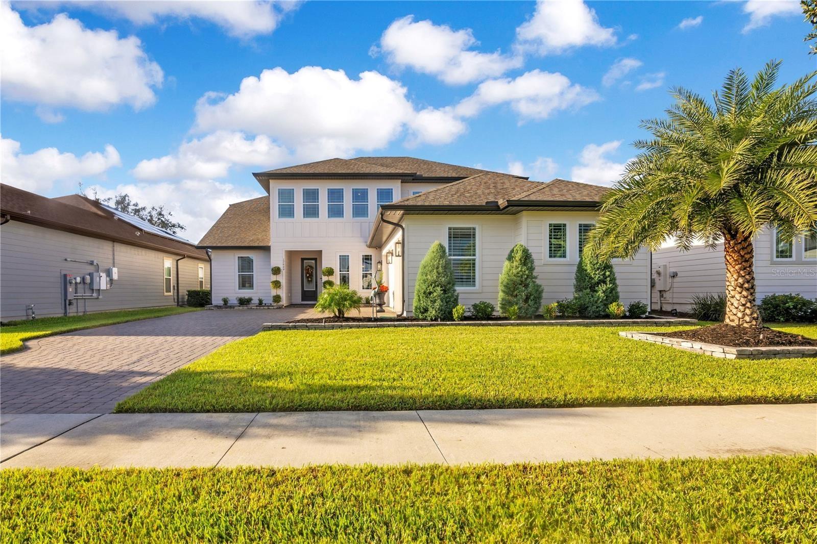 Beautiful two-story exterior featuring a paver driveway, manicured lawn and upgraded landscaping.