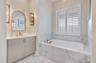 Elegant bathroom featuring a soaking tub, upgraded tile surrounds and a vanity accented by designer sconces.
