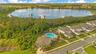 Aerial view of the community amenity area with a pool, clubhouse and lake backdrop.