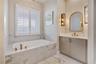 Relaxing bath retreat with a soaking tub beneath plantation shutters, decorative mirror and gold-tone fixtures.