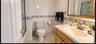 AI Enhanced Photo: Vitrually stagedBathroom featuring a wood-toned vanity with an integrated basin, white tile flooring, wall-mounted cabinetry with m
