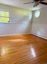 Bedroom featuring wood-finish flooring, white beadboard wainscoting, an octagonal window with decorative muntins, and a ceiling fan
