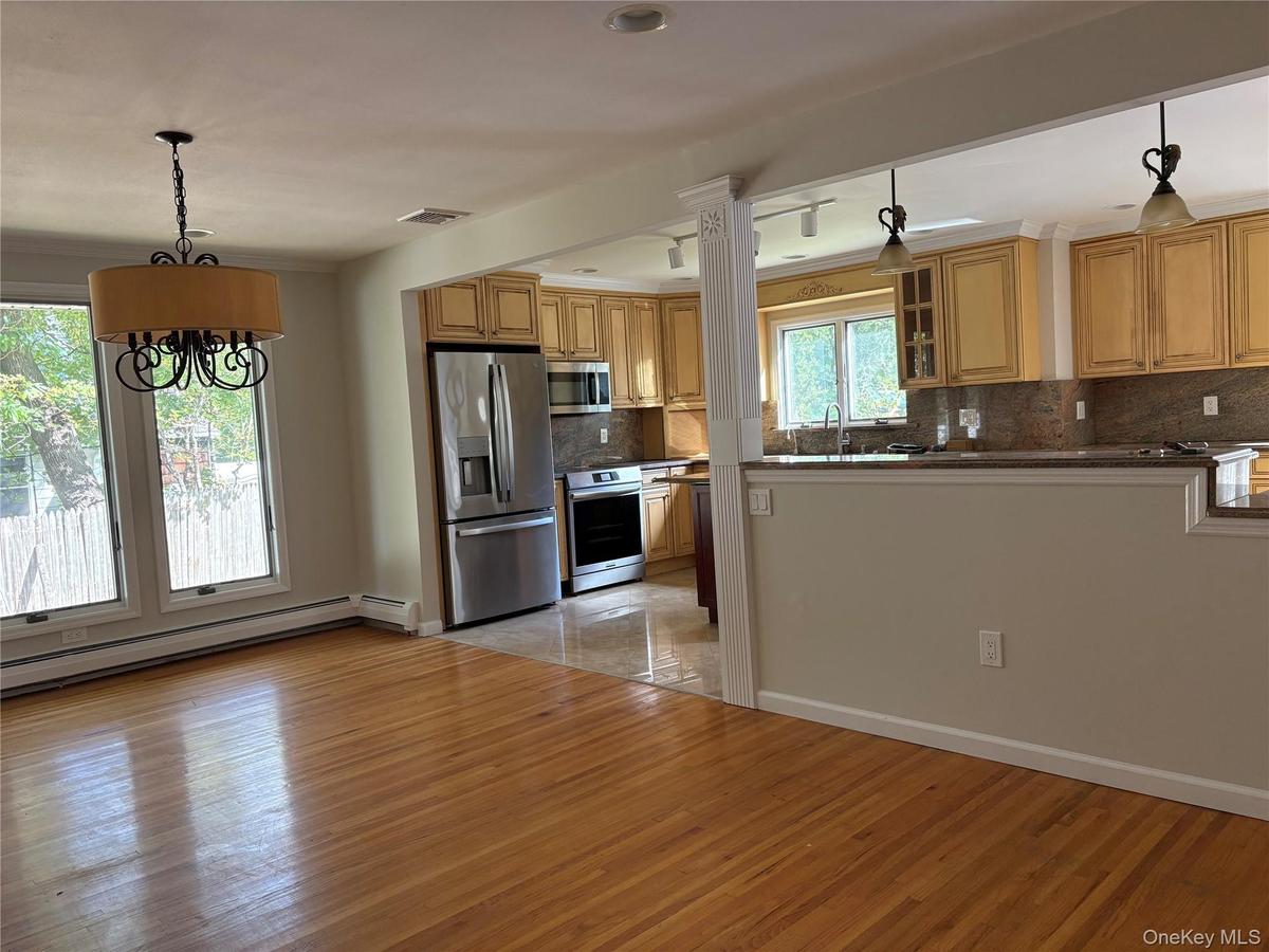 Dining area / kitchen featuring natural wood cabinetry, stone countertops, stainless steel appliances, wood-finish flooring, and a decorative pendant 