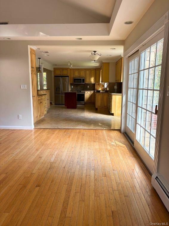 Hardwood flooring, vaulted ceilings, and glass-pane sliding patio doors leading to a kitchen with wood cabinetry and tile flooring