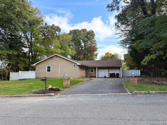 Ranch-style residence featuring horizontal siding, an attached garage, stone-accented driveway entrance pillars, and white vinyl privacy fencing