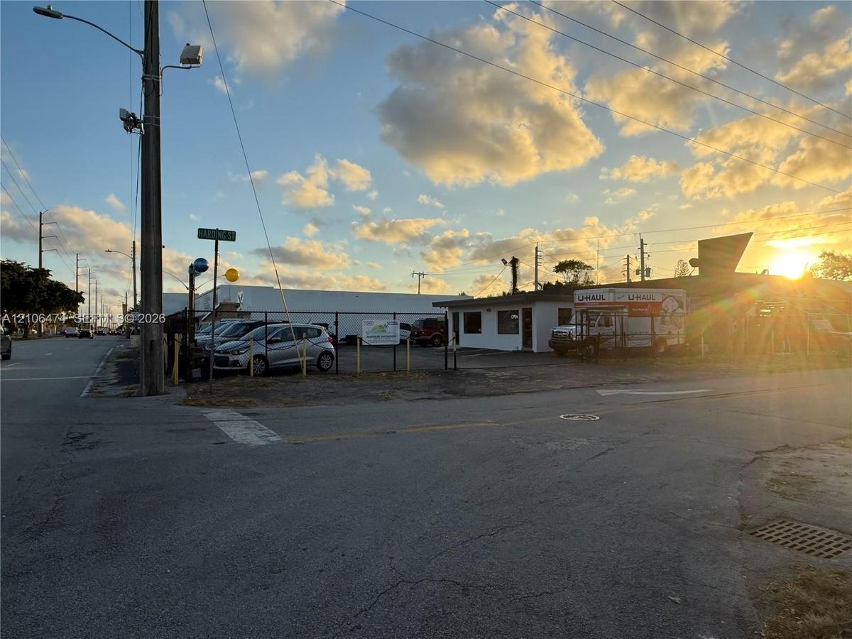 Corner lot property featuring a paved asphalt surface, perimeter chain-link fencing, and a single-story commercial structure