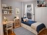 Light-filled bedroom featuring wood-finish flooring, a double window with white trim, built-in shelving, and a white bi-fold closet (virtually staged)