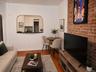 Exposed brick accent wall, wood-finish flooring, and a kitchen pass-through with a dark countertop (virtually staged)