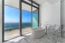 Freestanding soaking tub with a floor-mounted faucet, expansive floor-to-ceiling glass sliding doors, stone wall and floor surfacing, and an attached 