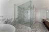 Walk-in glass-enclosed shower featuring floor-to-ceiling stone tile, freestanding soaking tub, dual-sink vanity with wood-finish cabinetry, and stone 