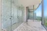 Full-height stone wall cladding, floor-to-ceiling glass paneling, frameless glass shower enclosure with dual rainfall showerheads, and a freestanding 