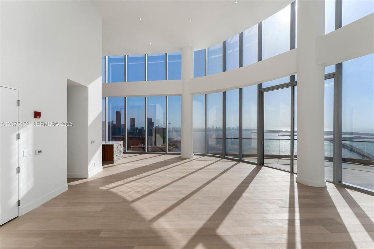 Curved floor-to-ceiling glass curtain wall, wood-finish flooring, recessed ceiling lighting, and structural cylindrical columns