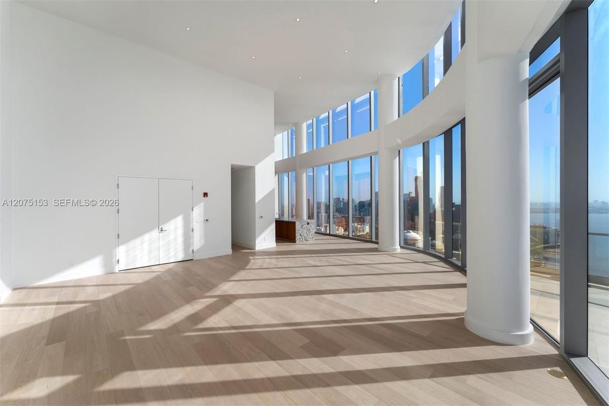 Open-concept interior featuring floor-to-ceiling curved glass windows, wood-finish flooring, recessed lighting, and structural columns