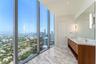 Floor-to-ceiling windows featuring panoramic urban scenery, dual-sink vanity with stone-surfaced countertop, wood-finish cabinetry, and large-format t