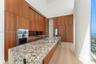 Kitchen featuring full-height wood-finish cabinetry, stone countertop island with integrated stainless steel sink, built-in stainless steel double wal