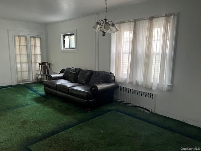 Living area featuring radiator heating unit, dark colored carpet, a chandelier, and french doors