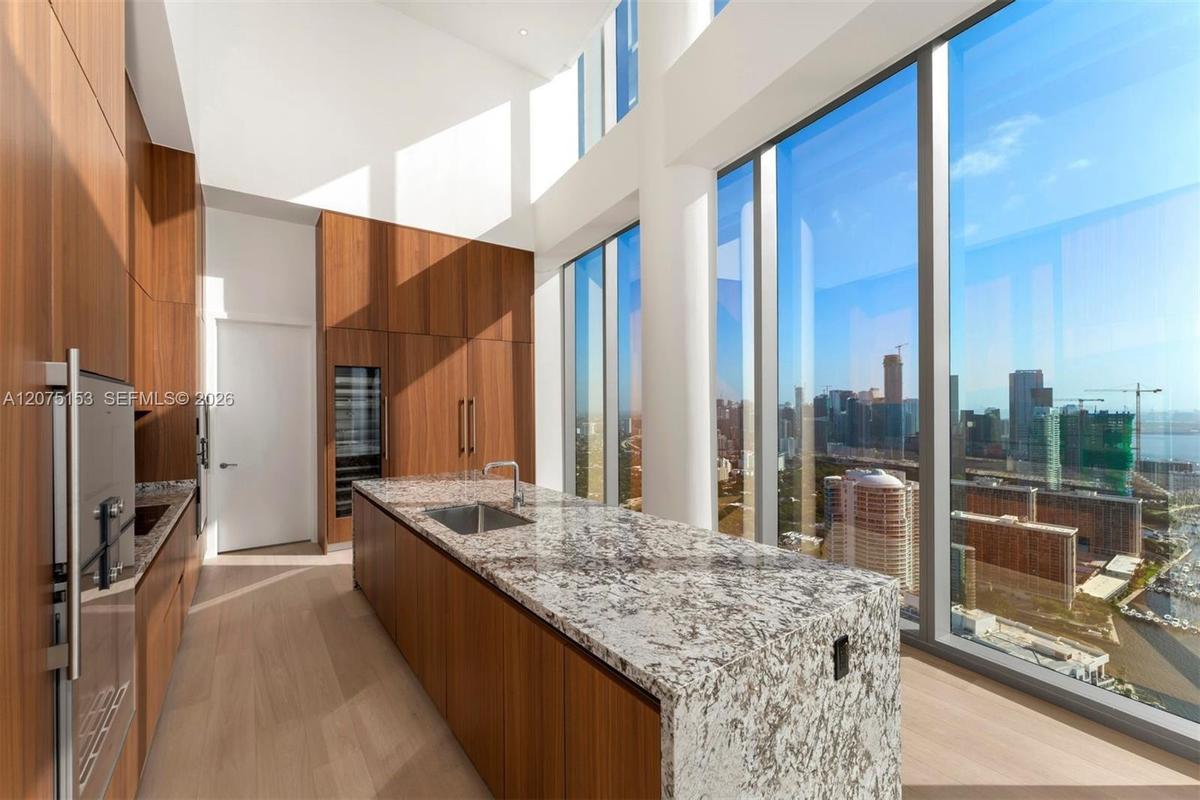 Gourmet kitchen featuring floor-to-ceiling cabinetry, stone waterfall island, integrated stainless steel appliances, and expansive double-height windo