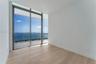 Floor-to-ceiling glass sliding doors, private balcony with glass railing, wood-finish flooring, and expansive water and city skyline backdrop