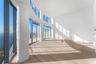 Floor-to-ceiling glass walls, curved architectural columns, double-height ceilings, recessed lighting, and wood-finish flooring