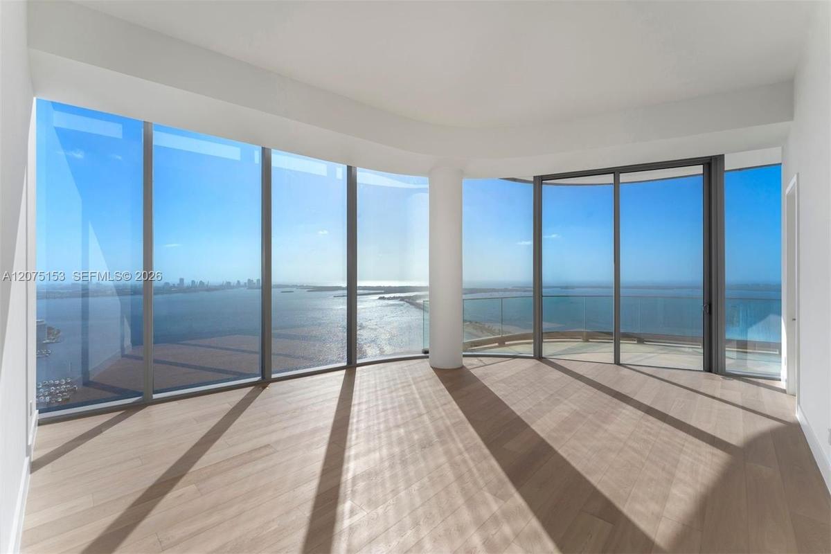 Floor-to-ceiling windows, wood-finish flooring, sliding glass door, glass-panel balcony railing, and water-fronting horizon