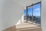 Floor-to-ceiling glass corner windows, wood-finish flooring, and a private glass-railed balcony with expansive urban and water scenery