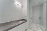 Bathroom featuring a stone-finish countertop with an integrated rectangular sink, wall-mounted linear light fixture, walk-in shower with glass enclosu