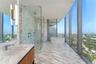 Floor-to-ceiling windows, natural stone surfaces, walk-in glass-enclosed shower with dual rainfall showerheads, and freestanding soaking tub