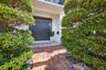 A distinguished entrance framed by lush Tropical Landscaping with beautiful brick paver steps lead to an elegant, natural stone, Landing and impressiv