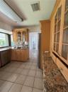 Kitchen featuring light-finish cabinetry with glass-panel upper doors, stone-surface countertops, stone-pattern backsplash, stainless steel dishwasher