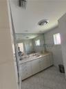 Bathroom vanity featuring solid-surface countertop with an integrated basin, white cabinetry, expansive wall-to-wall mirror, polished metal fixtures, 