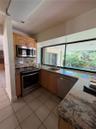 Kitchen featuring natural wood cabinetry, stone countertops, stainless steel appliances, tile flooring, and a large window