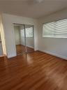 Room featuring wood-finish flooring, mirrored sliding closet doors, and windows with horizontal blinds