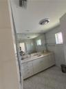 Bathroom featuring a solid-surface vanity with an integrated sink, expansive wall-to-wall mirror, neutral tile flooring, and metallic wall-mounted tow