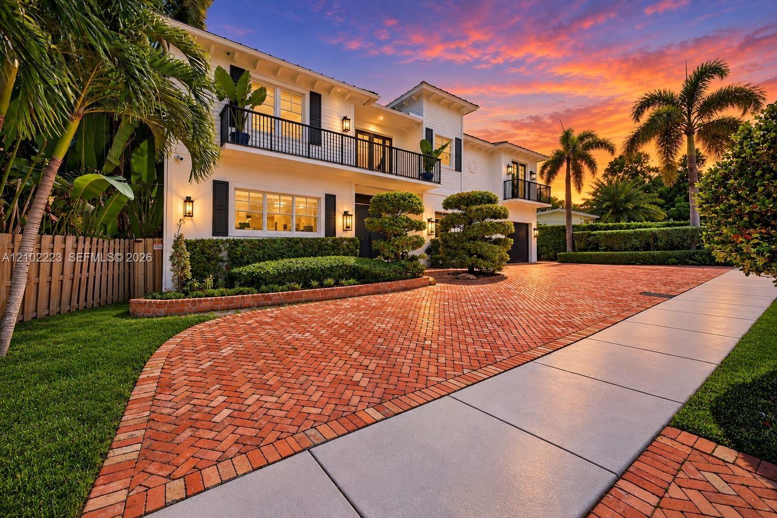 Two-story exterior featuring 2 car garage, circular drive, black balcony railings, a herringbone-patterned brick driveway, manicured landscaping, and 