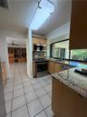 Kitchen featuring light-finish wood cabinetry, stone countertops, stainless steel appliances, tile flooring, and a large horizontal window