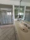 Vanity with a solid-surface countertop and integrated sink, full-width mirror, tile flooring, and a shower-tub combination with a sliding glass door