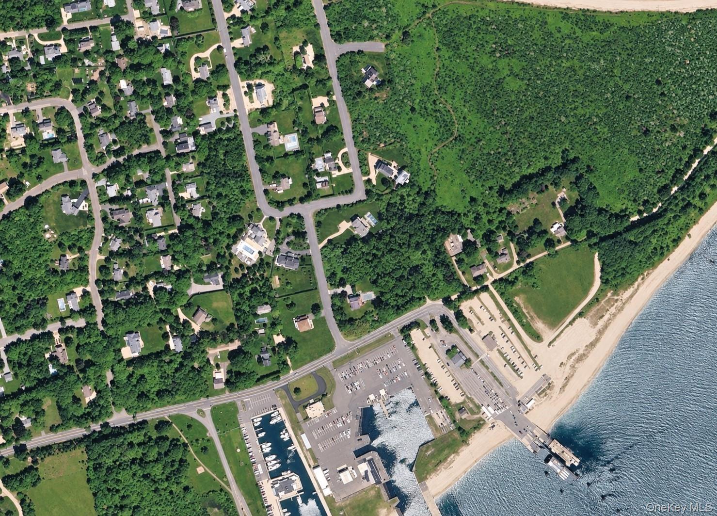 Aerial perspective featuring coastal proximity, dense woodland buffers, paved road infrastructure, and an established marina