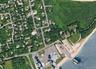 Aerial perspective featuring coastal proximity, dense woodland buffers, paved road infrastructure, and an established marina